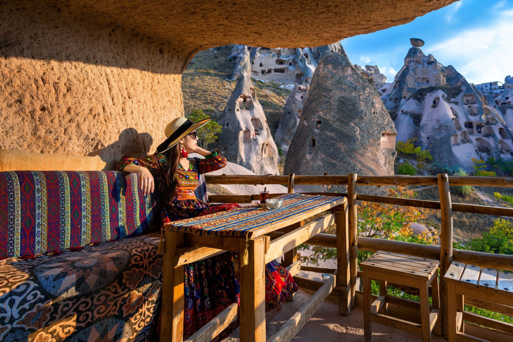 A woman in a colorful bohemian dress and a wide-brimmed hat relaxes on a traditional terrace of a Best Hotels in Cappadocia Turkey Cappadocia,